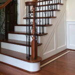 New stair renovation completed by Darby Stair Renovations featuring finished wood treads, painted white risers, and decorative wrought iron railings.