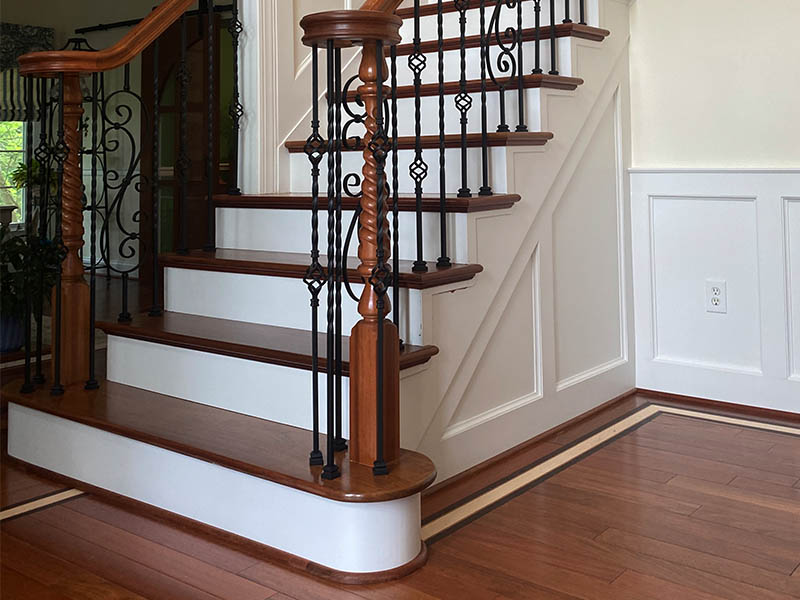 New stair renovation completed by Darby Stair Renovations featuring finished wood treads, painted white risers, and decorative wrought iron railings.