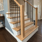 Completed staircase renovation featuring light stained wood and wrought iron balusters.