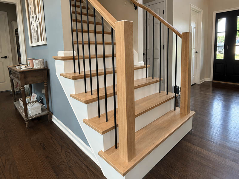 Completed staircase renovation featuring light stained wood and wrought iron balusters.
